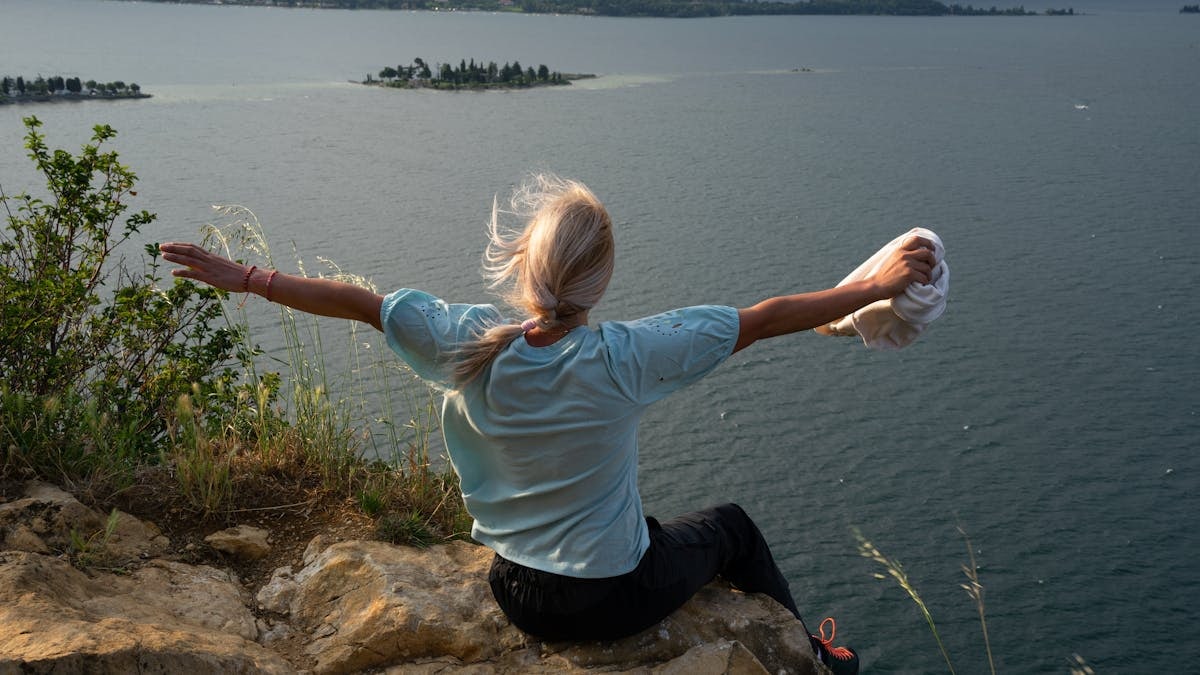 Woman enjoys a breathtaking lake view from a cliff at sunset, exemplifying freedom and adventure.